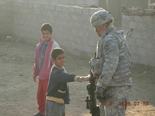 Cody Rose in uniform on deployment in Iraq, greeting two local children.