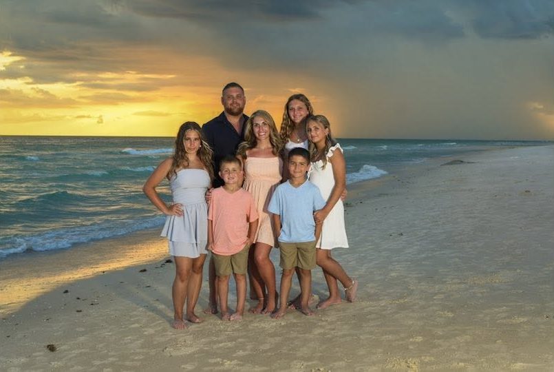Cody Rose with his family on a beach at sunset, storm clouds over the water behind them.