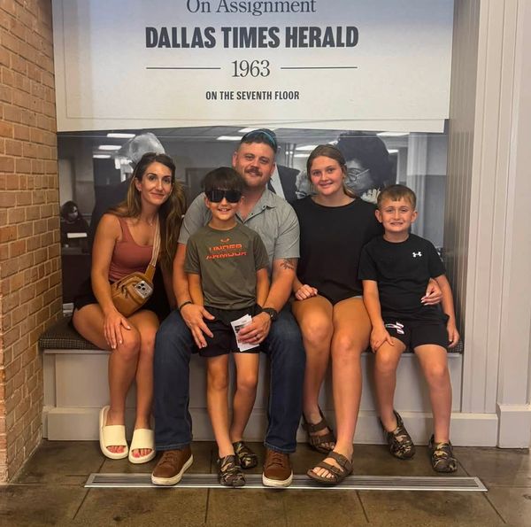 Cody Rose with his family on a bench beneath the Dallas Times Herald 1963 exhibit in Dallas.