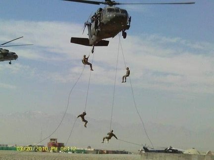 Soldiers rappelling on ropes from a hovering Black Hawk helicopter, mountains in the distance.
